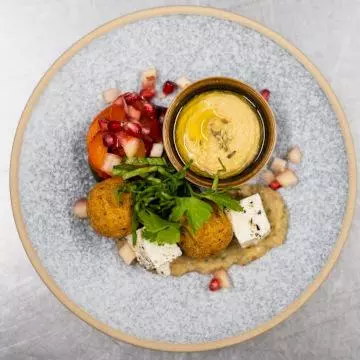 Photo of a Mediterranean themed starter for a formal dinner, with hummus, falafel, feta and pomegranate seeds
