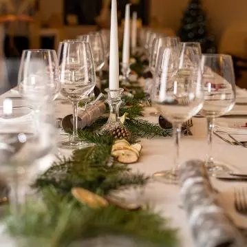 Photo of a table laid for a formal dinner with wine glasses, candles and greenery