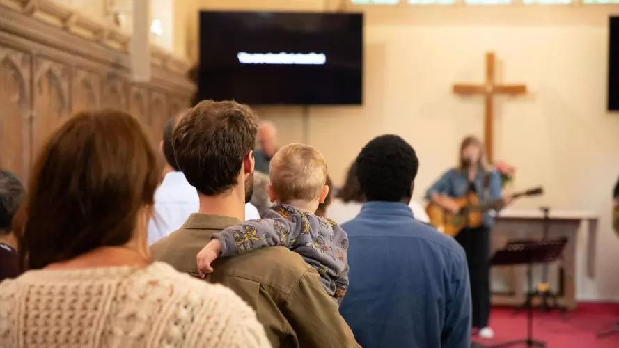 Audience worshipping in Wycliffe Chapel, with two men, one woman and a child in front of the cross