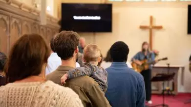 Audience worshipping in Wycliffe Chapel, with two men, one woman and a child in front of the cross